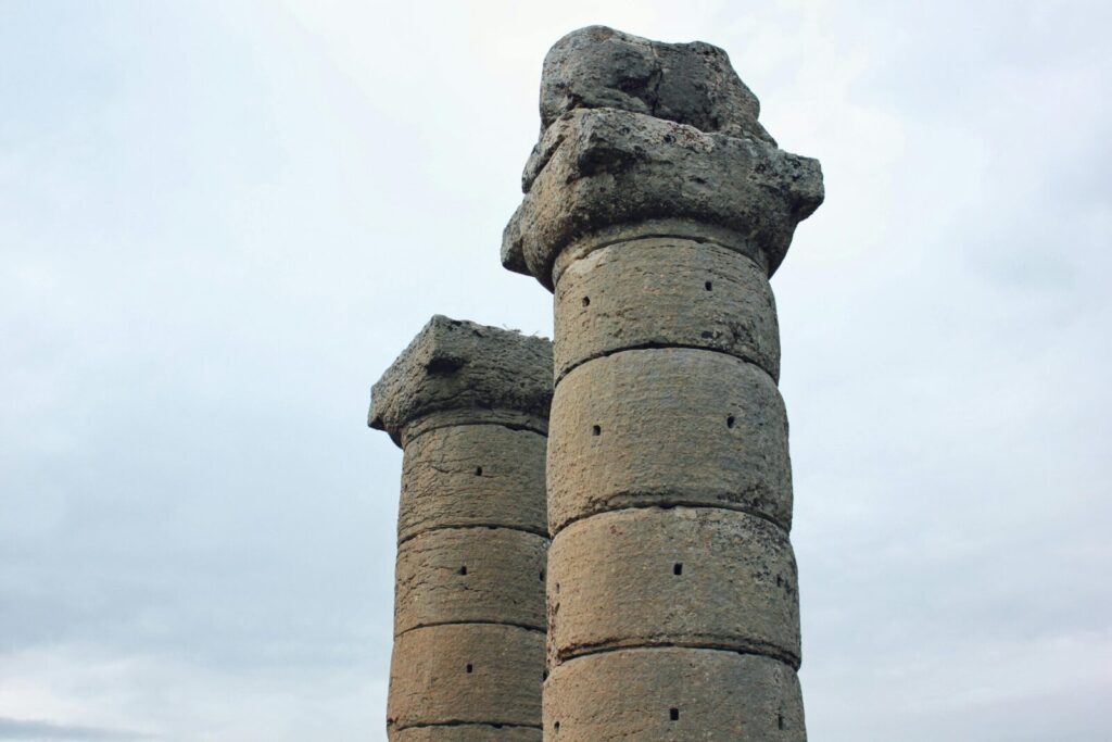 Ancient stone columns against a cloudy sky in Adıyaman, Türkiye, showcasing historical architecture.